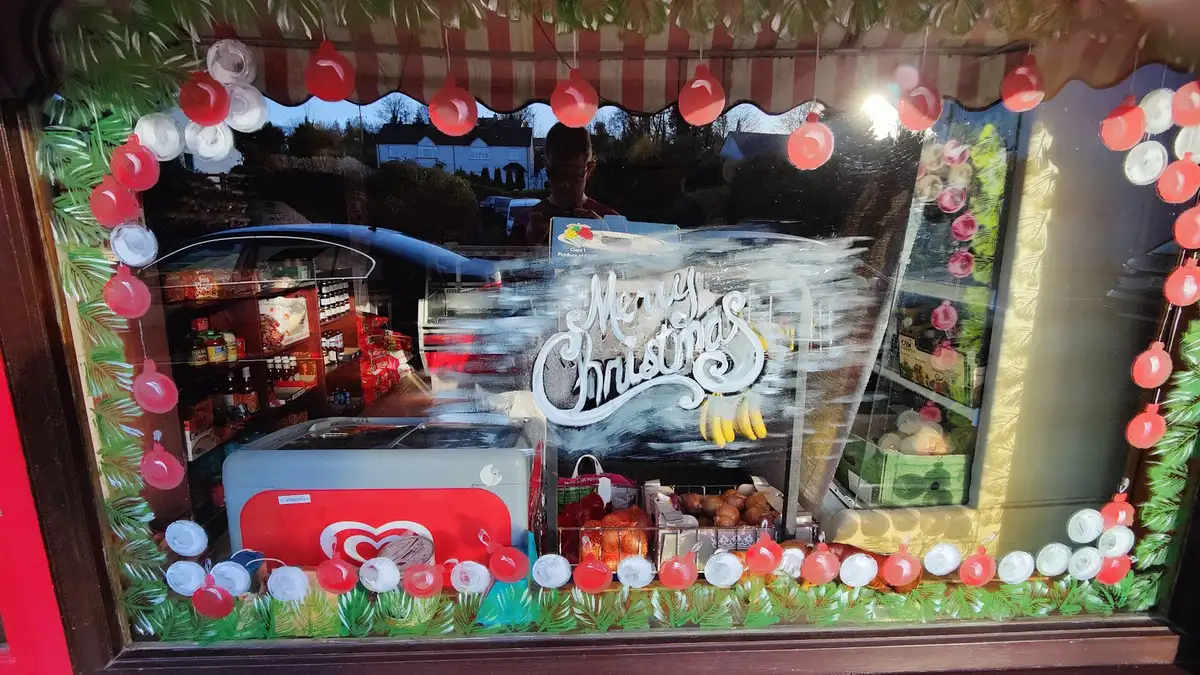 Looking through the painted shop window at the shelves, produce and freezer inside