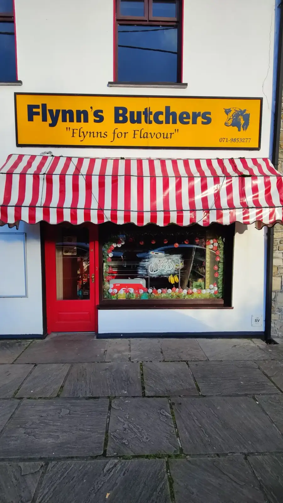 The Flynn's Butchers shopfront - chrome yellow fascia sign with navy lettering, red and white striped awning and red door